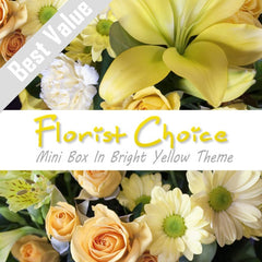 A bright yellow mini box of fresh seasonal flowers, arranged with greenery for a cheerful surprise.