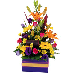 A vibrant box arrangement of roses, lilies, gerberas, lisianthus, and chrysanthemums with tropical foliage in mixed colors.