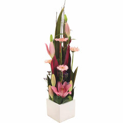 A modern pink ceramic container with gerberas, lilium, statice, and tropical leaves for a stylish look.