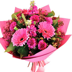 A soft pink bouquet of gerberas, carnations, and stock with beech and greenery for a charming look.