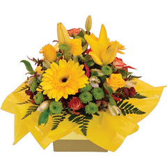 A vibrant yellow and orange mini box of roses, gerberas, lilium, and alstroemeria with chrysanthemums and greenery.