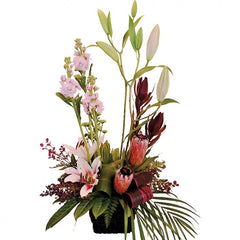 A lush pink and green basket of oriental lilies, stock, protea, and leucadendron with tropical foliage and berries.