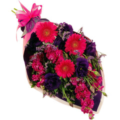 A sleek purple and pink sheath bouquet of mini gerberas, lisianthus, spray carnations, and statice with greenery.