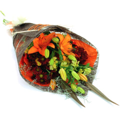 A fiery orange and red sheath bouquet of lilies, chrysanthemums, and Singapore orchids with flax leaves and misty.