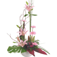 A modern pink ceramic container with lilium, mini gerberas, twigs, and tropical foliage for a chic look.