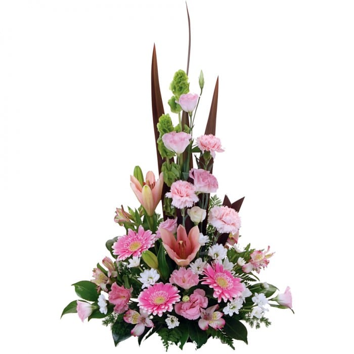 A pastel pink, white, and green A-line arrangement of lisianthus, mini gerberas, lilies, and alstroemeria with foliage.