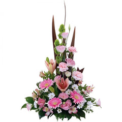 A pastel pink, white, and green A-line arrangement of lisianthus, mini gerberas, lilies, and alstroemeria with foliage.