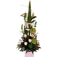 A lush ceramic container with white and green roses, anthuriums, snapdragons, and mini gerberas with tropical foliage.